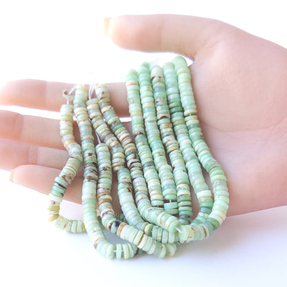 A person holds delicate strands of Chrysoprase smooth wheel beads, showcasing their polished design.