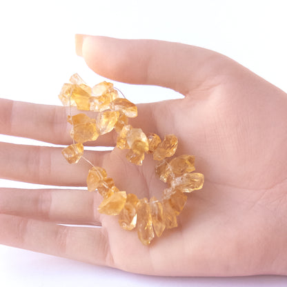 A person holds delicate pieces of Citrine rough beads, showcasing their drilled rough design.
