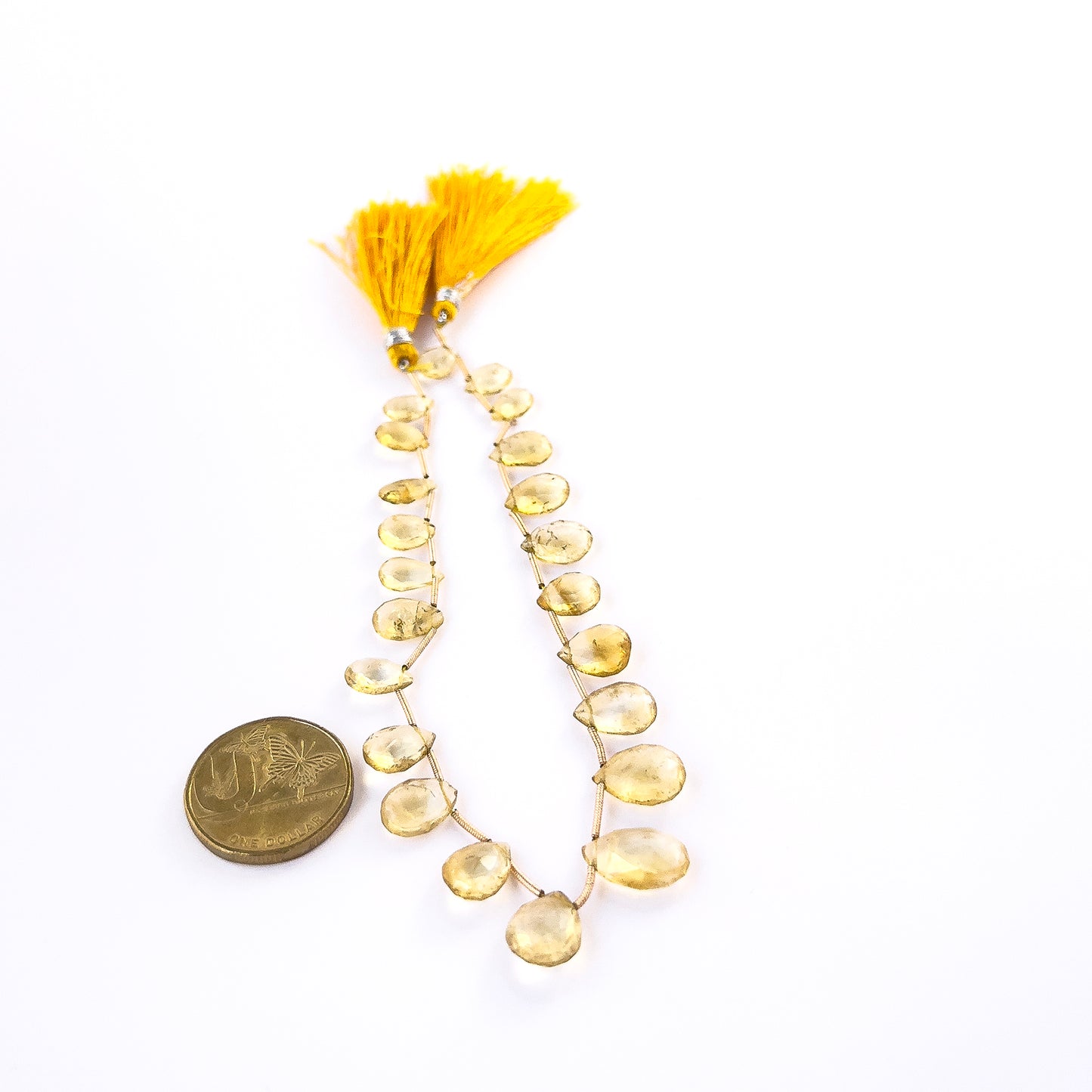 A coin is placed near delicate pieces of Citrine faceted briolette beads for scale.