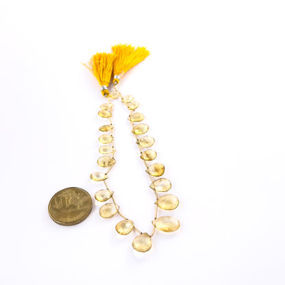 A coin is placed near delicate pieces of Citrine faceted briolette beads for scale.