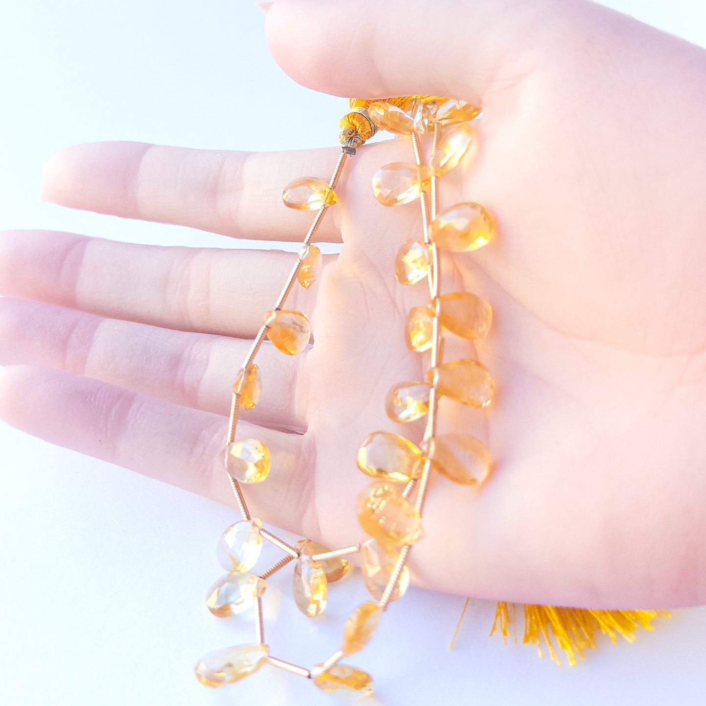 A person holds delicate strands of Citrine beads, showcasing their faceted briolette design.