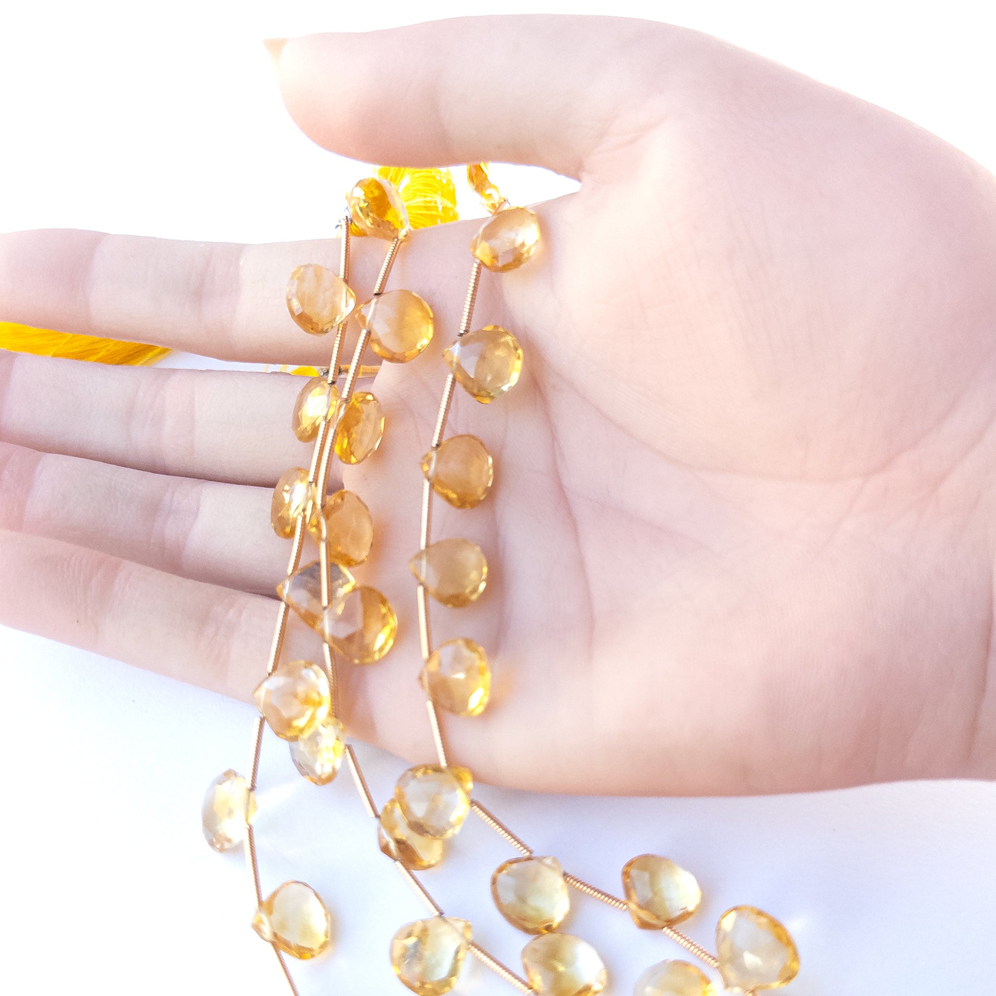 A person holds delicate strands of Citrine beads, showcasing their faceted briolette design.