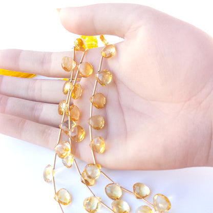A person holds delicate strands of Citrine beads, showcasing their faceted briolette design.