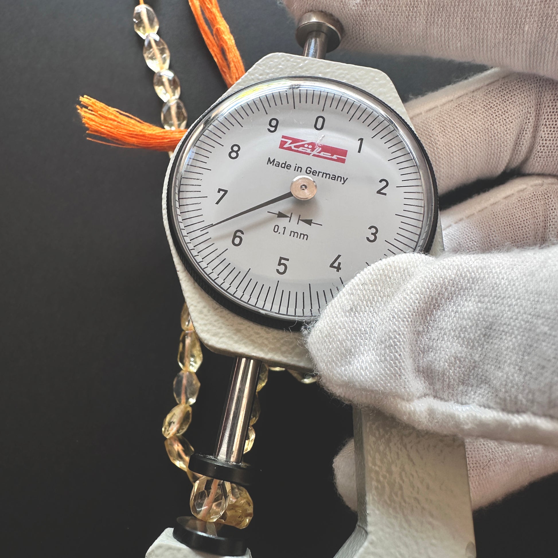 A dial gauge measures the Citrine faceted oval gemstone's length.