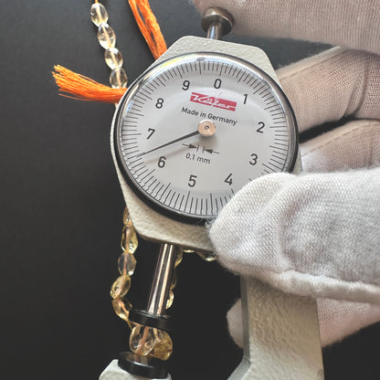 A dial gauge measures the Citrine faceted oval gemstone's length.
