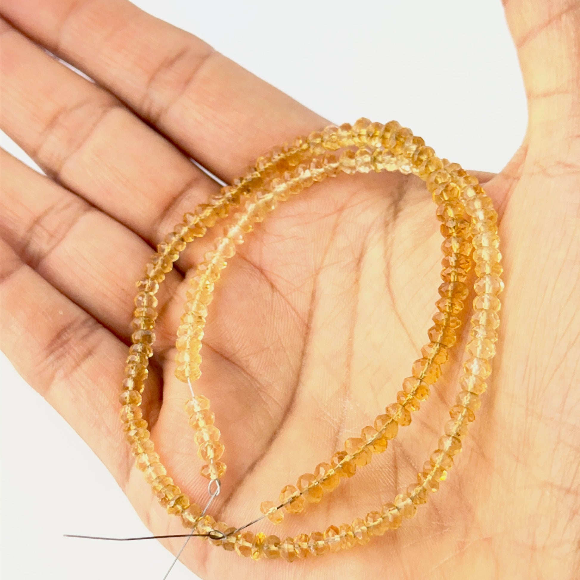 A person holds delicate strands of Citrine beads, showcasing their faceted rondelle design.