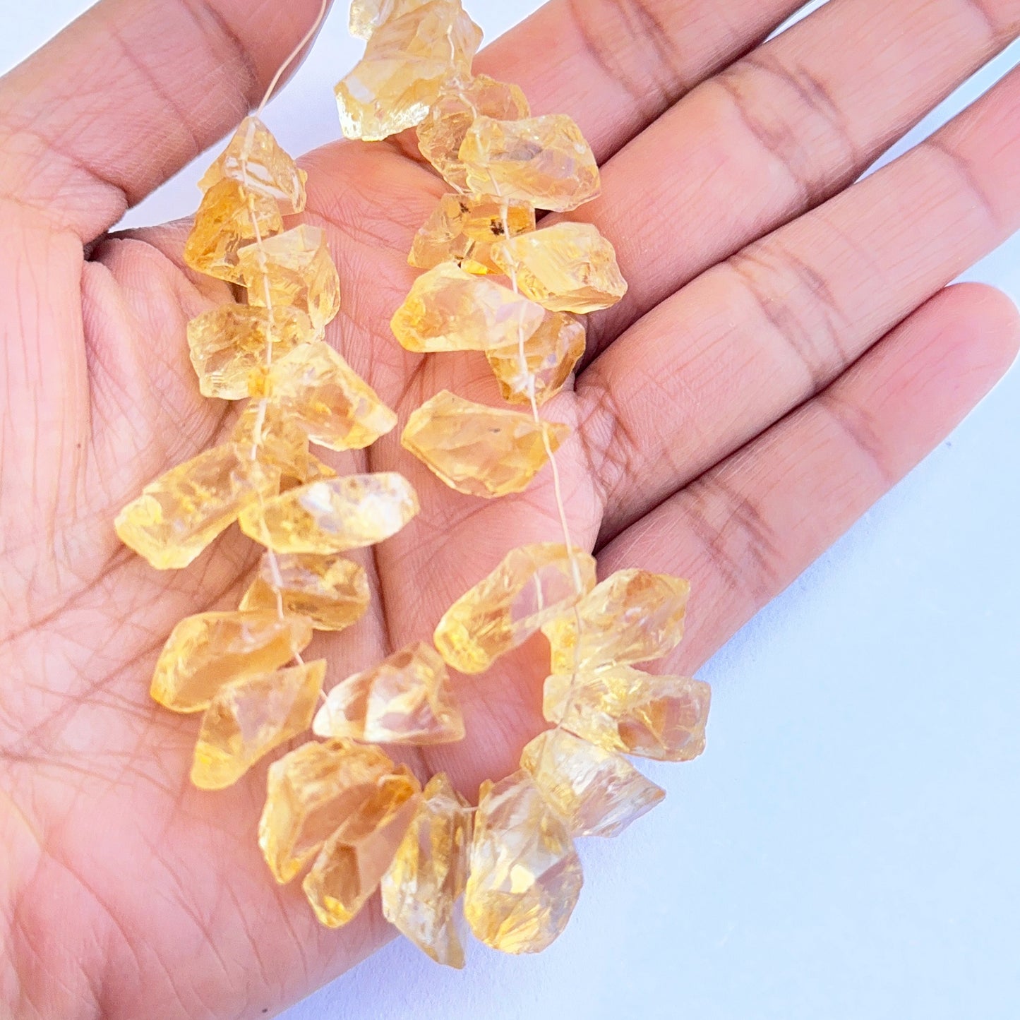 A person holds delicate strands of citrine beads, showcasing their smooth design