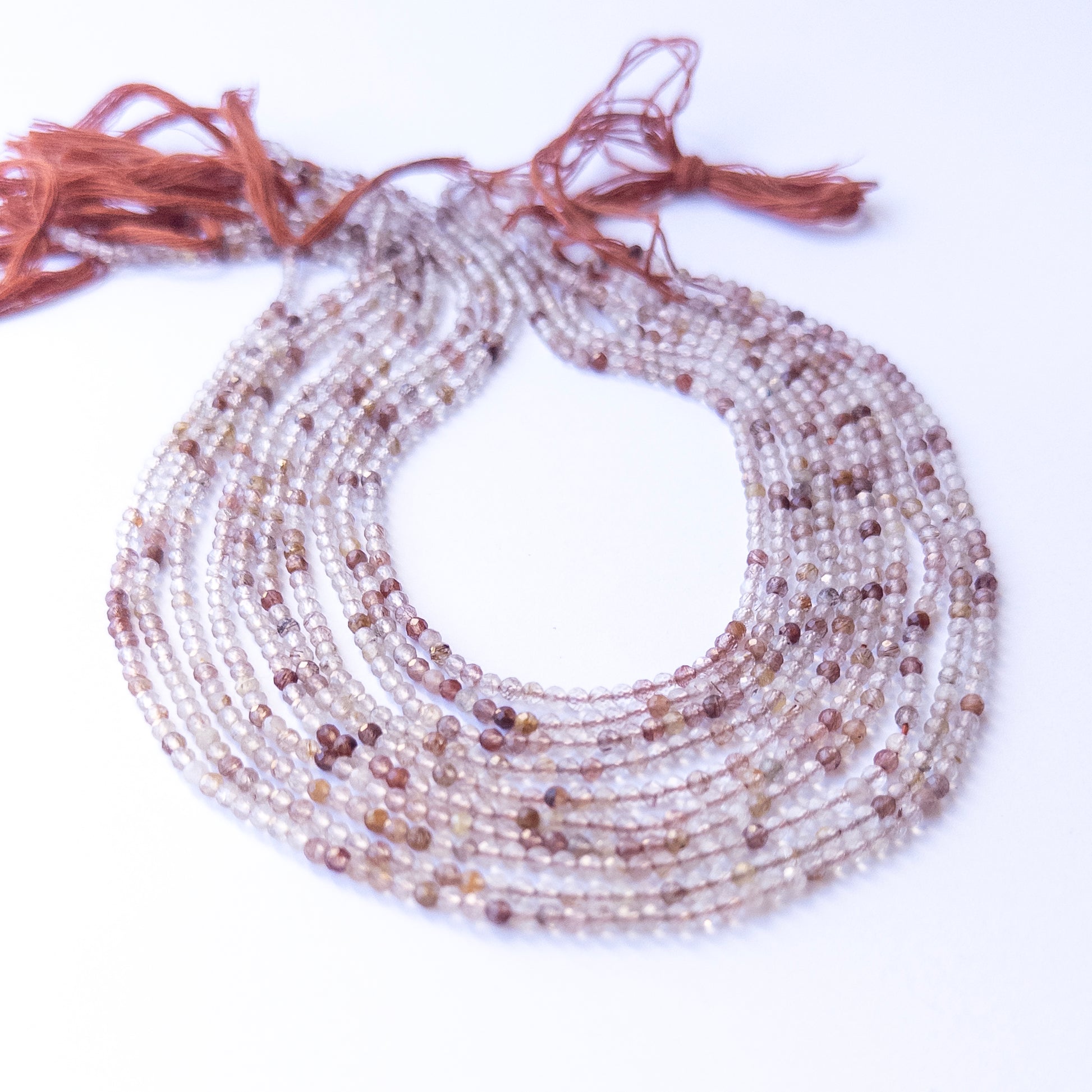 A person holds delicate strands of Copper Rutile beads, showcasing their faceted rondelle design.