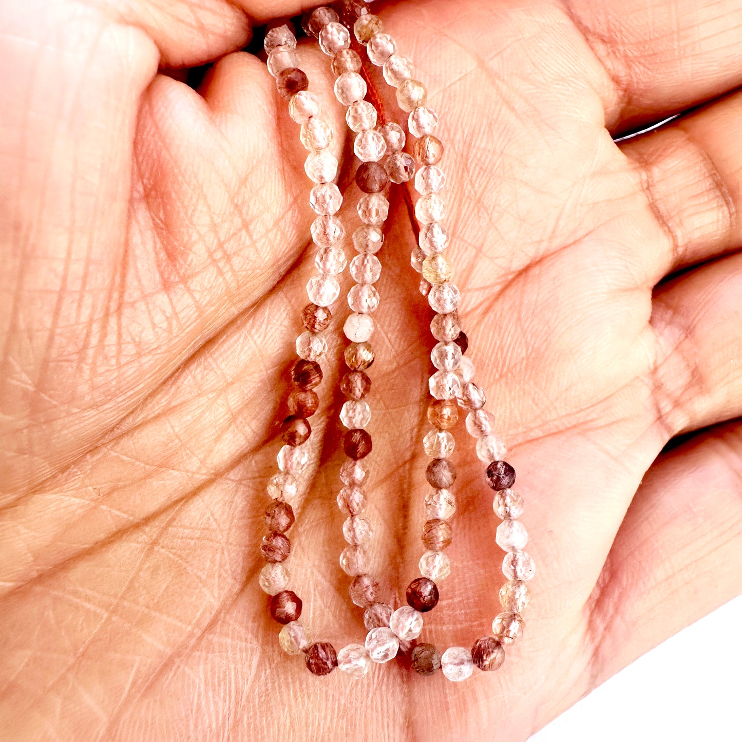 A person holds delicate strands of Copper Rutile beads, showcasing their smooth design.