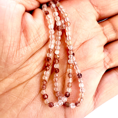 A person holds delicate strands of Copper Rutile beads, showcasing their smooth design.