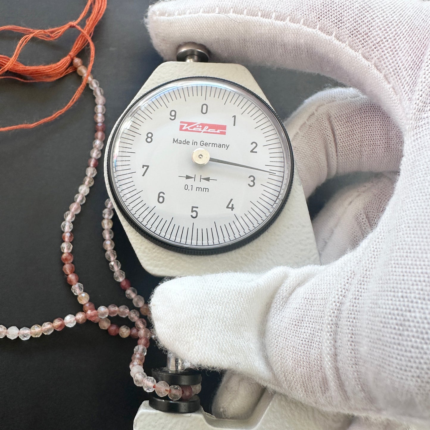 A dial gauge measures the Copper Rutile micro faceted rondelle 2.7mm gemstone.