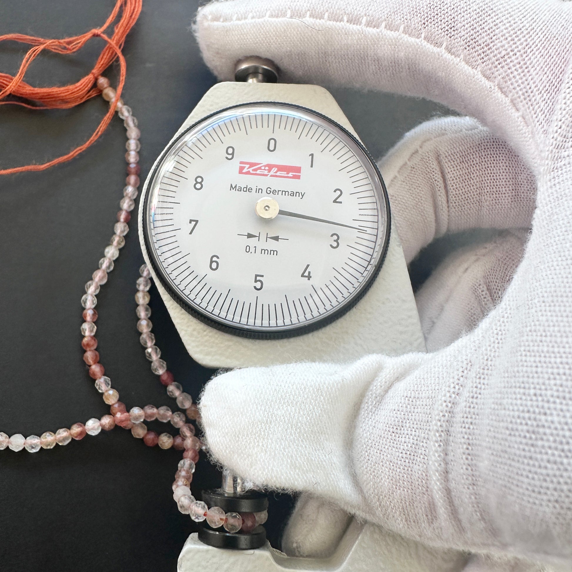 A dial gauge measures the Copper Rutile micro faceted rondelle 2.7mm gemstone.