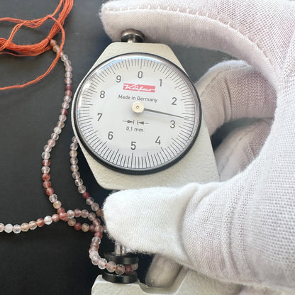 A dial gauge measures the Copper Rutile micro faceted rondelle 2.7mm gemstone.