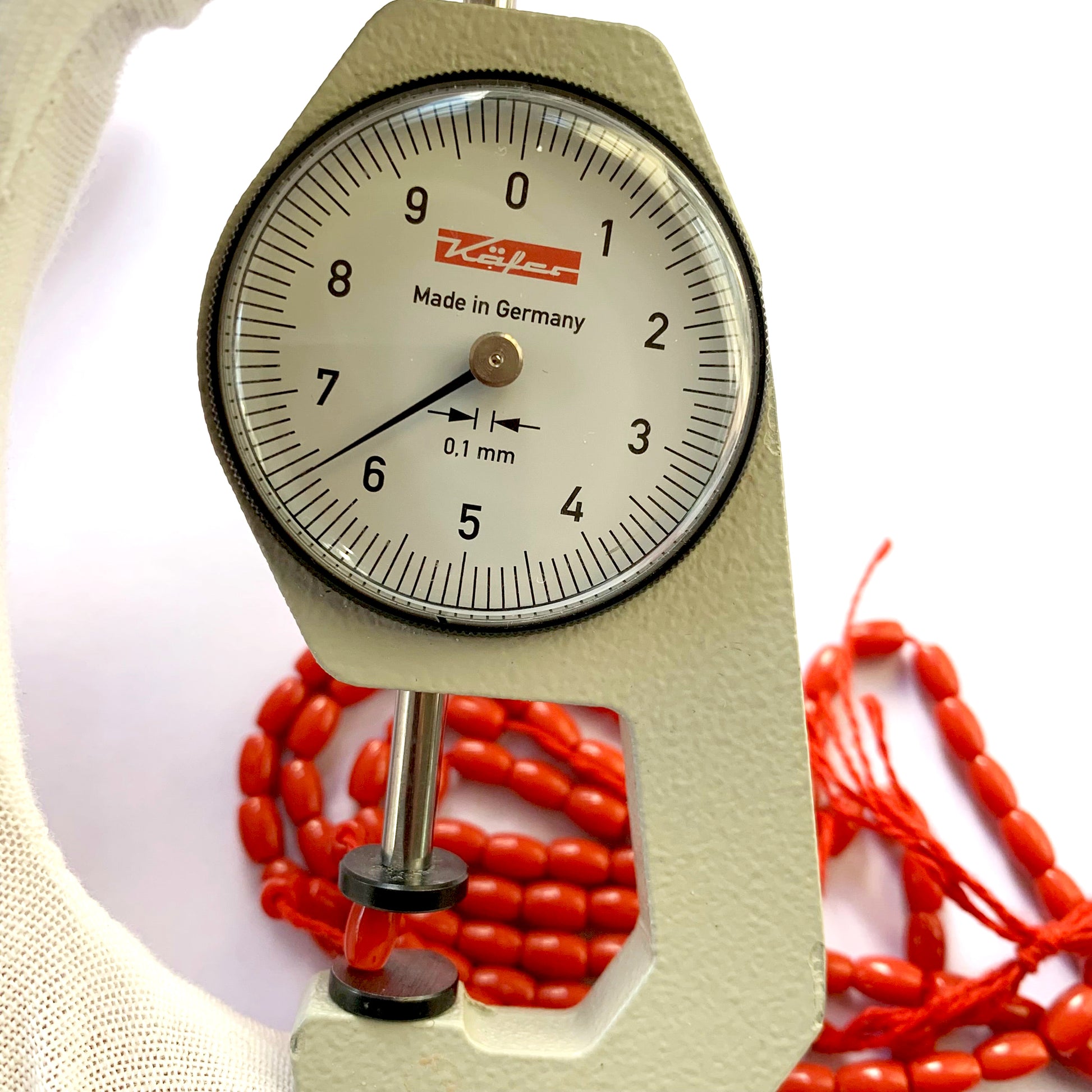 A dial gauge measures the Coral drum cut 6.7x4.4mm gemstone.