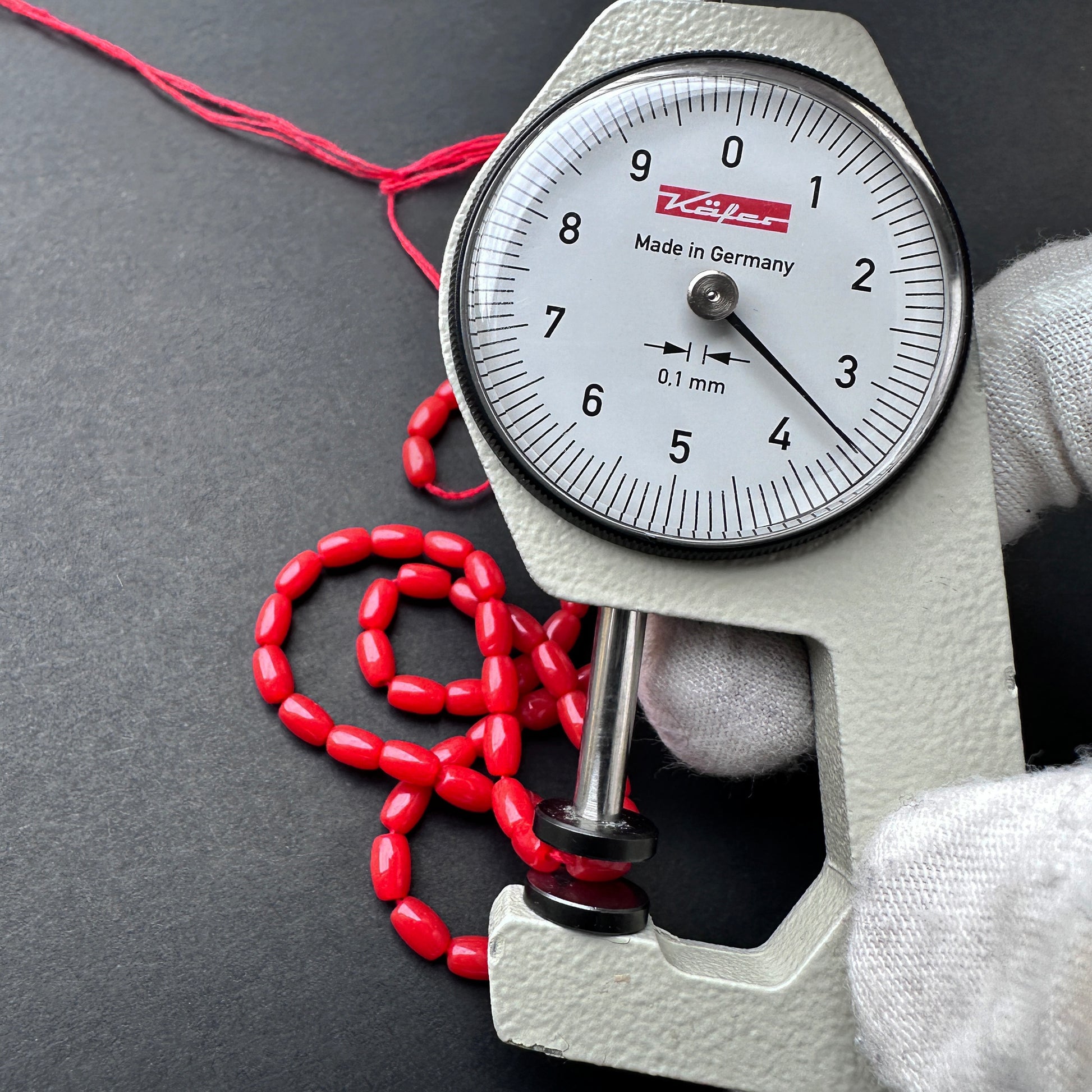 A dial gauge measures the Coral smooth drum 5.5 ‚àö√≥ 3.5mm gemstone.