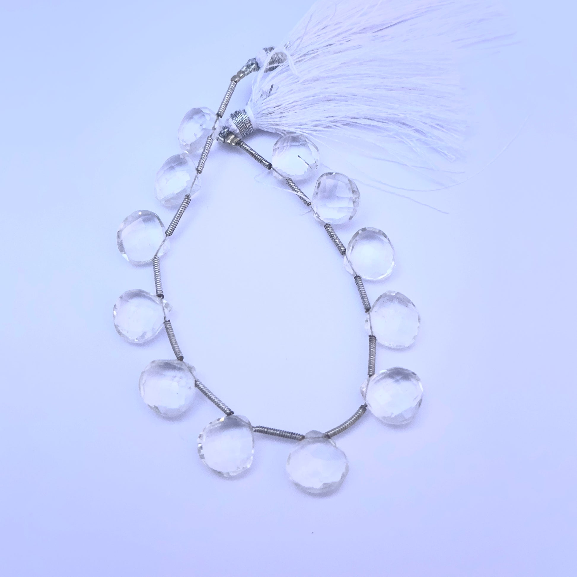 Crystal faceted heart briolette gemstone beads arranged in a circular strand with tassel accents.