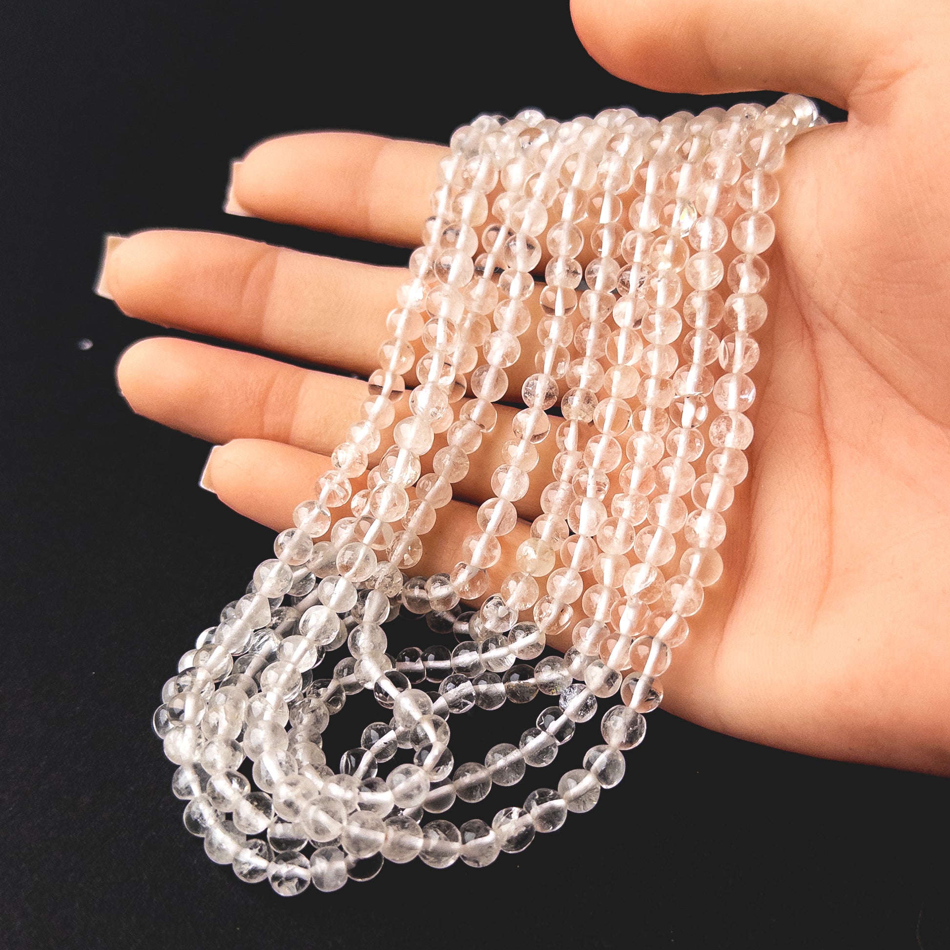 A person holds delicate strands of Crystal beads, showcasing their smooth round design.