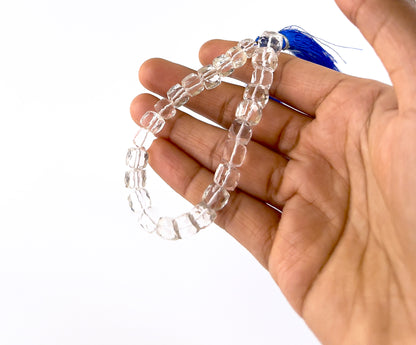 A person holds crystal smooth square beads, showing their polished shape and clear transparency.