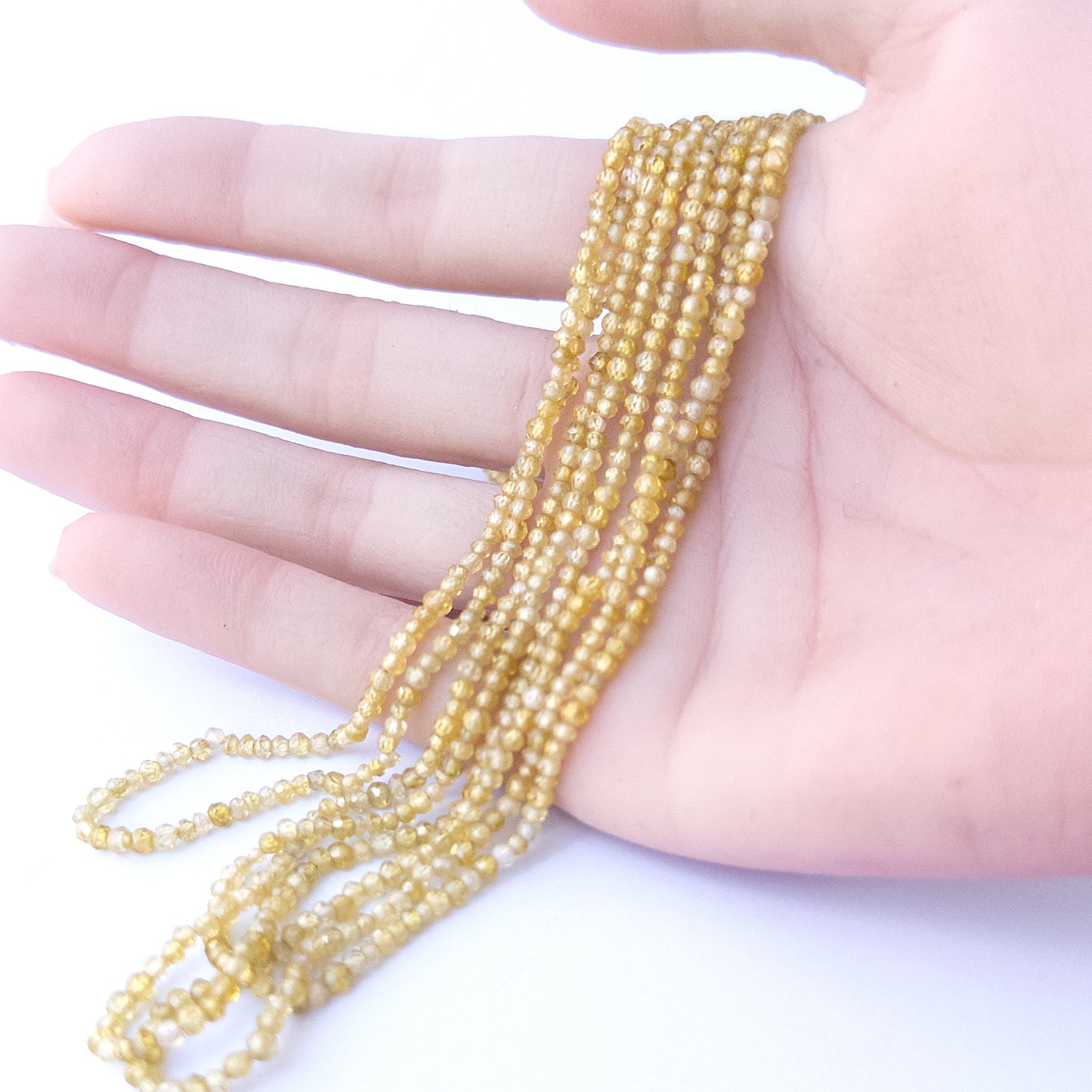 A person holds delicate strands of Cubic Zirconia beads, showcasing their faceted rondelle design.