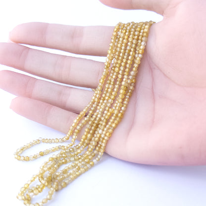 A person holds delicate strands of Cubic Zirconia beads, showcasing their faceted rondelle design.