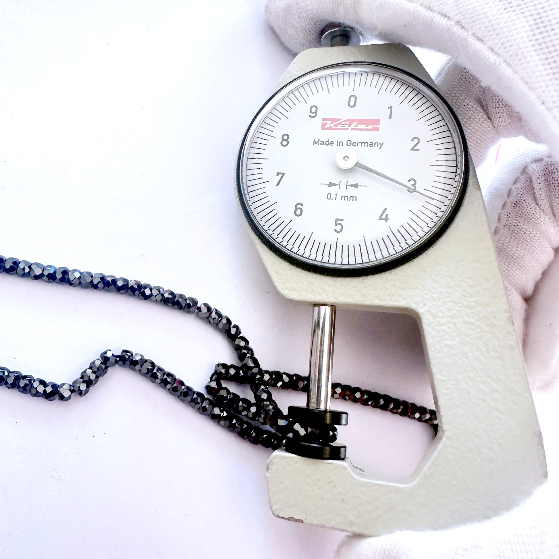 A dial gauge measures the Black Cubic Zirconia faceted rondelle 3mm gemstone.