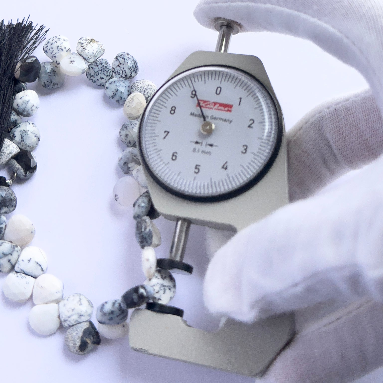A dial gauge measures the Dendrite Opal faceted briolette 8.5–8.7mm gemstone.