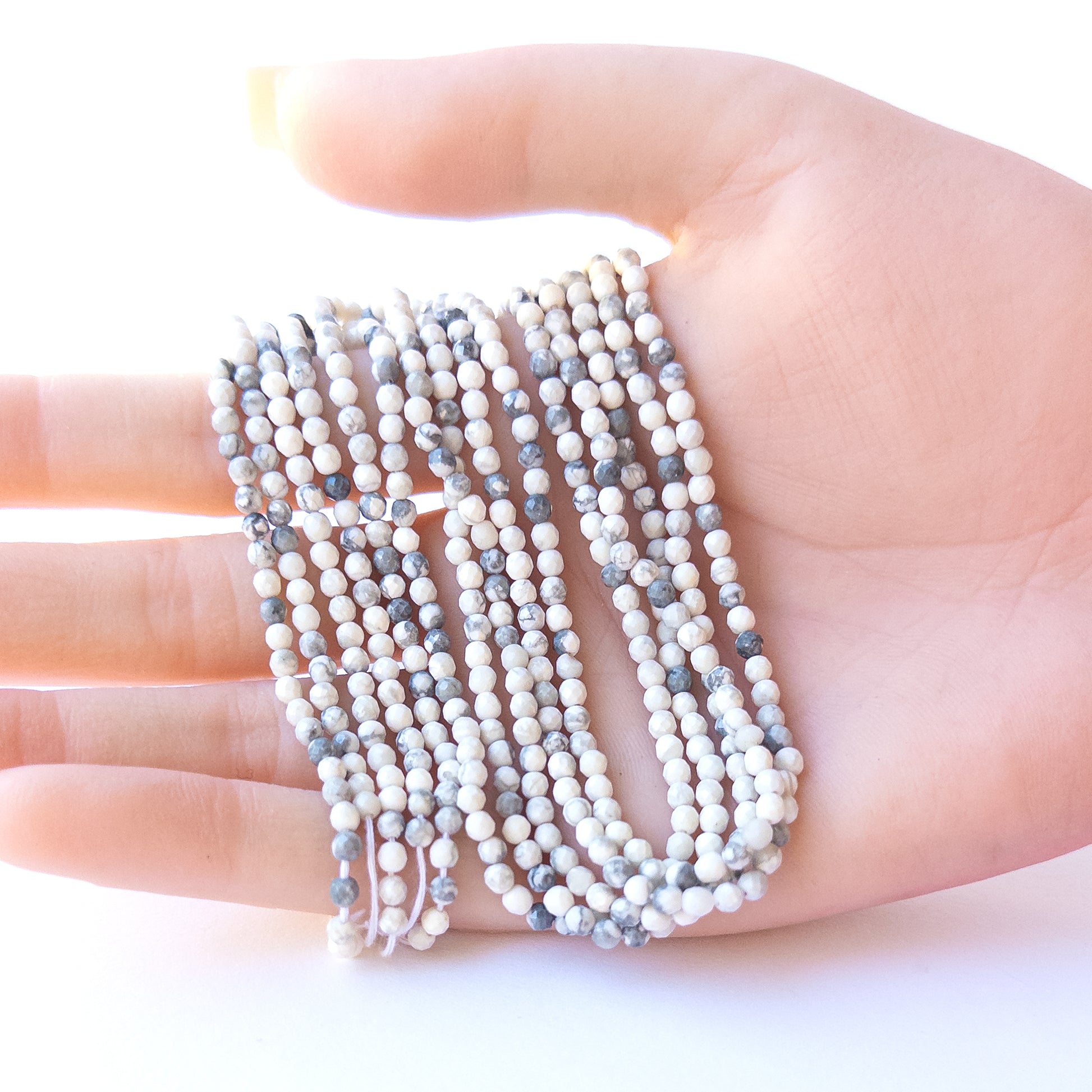 A person holds delicate strands of Dendrite Opal beads, showcasing their faceted rondelle design.