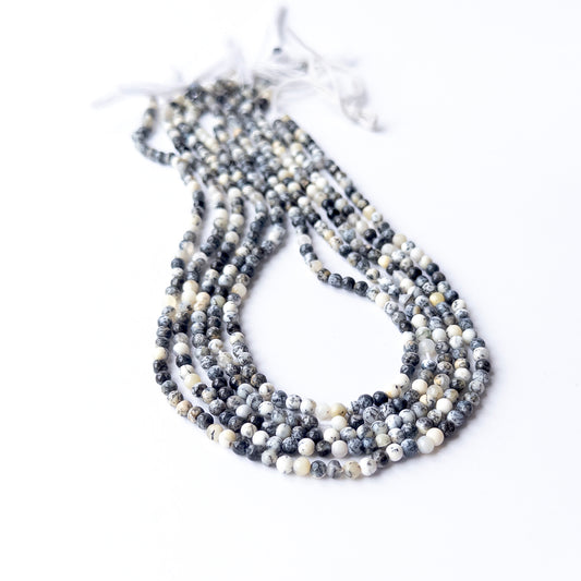 Strands of Dendrite Opal smooth round gemstone beads arranged neatly, showcasing their smooth finish and unique dendrite markings.