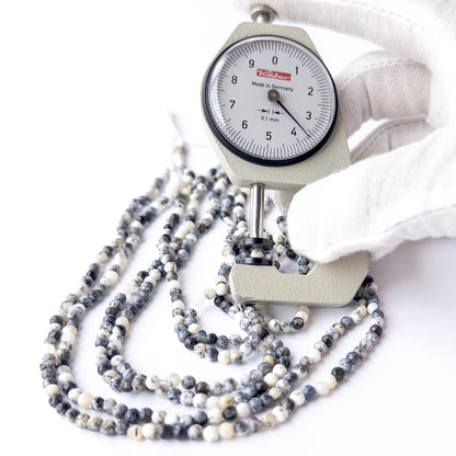 A person holds delicate strands of Dendrite Opal beads, showcasing their smooth round design.