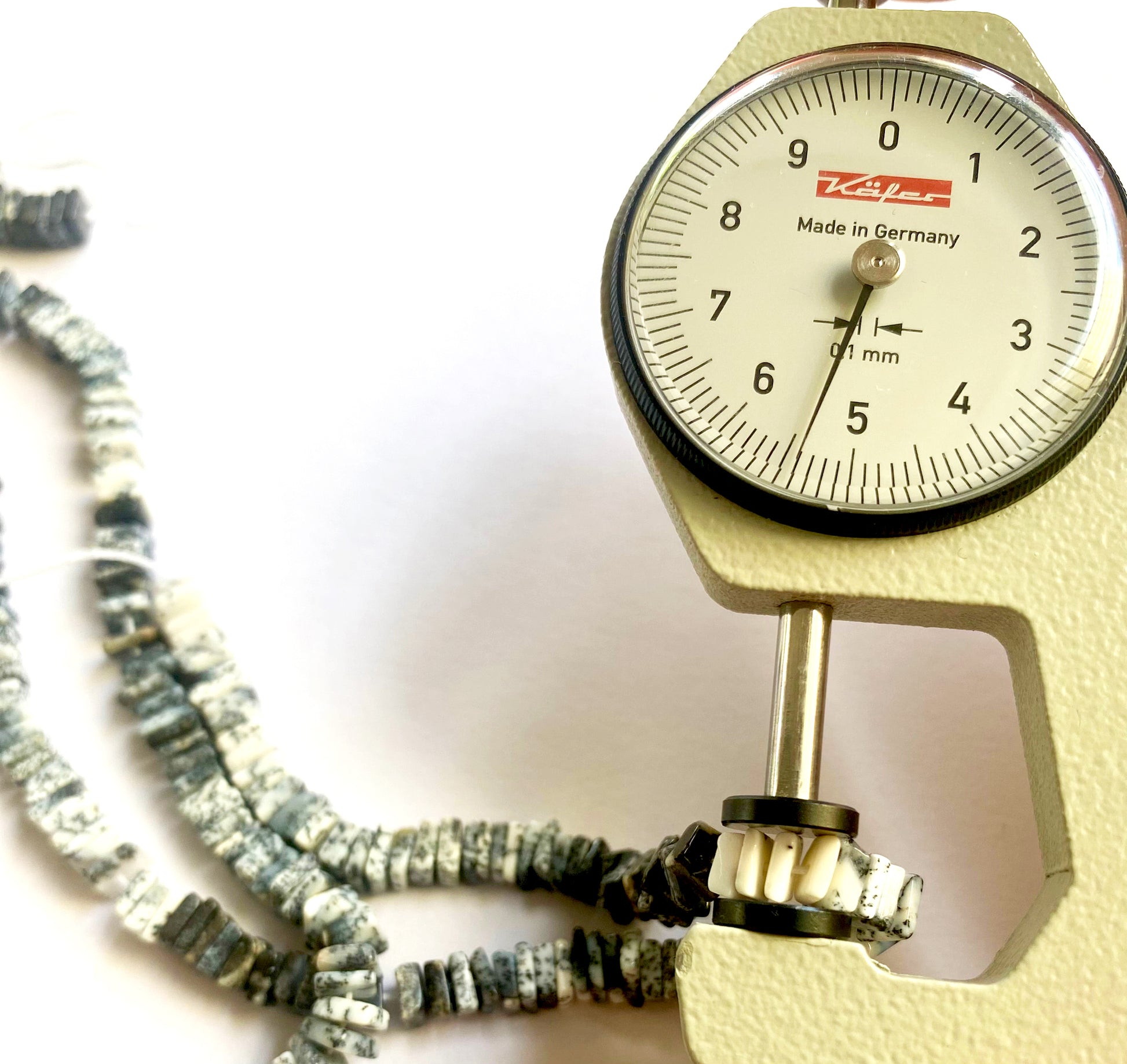 A dial gauge measures the Dendrite Opal Square Heishi 5.3-5.5mm gemstone.