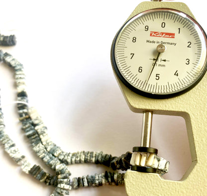 A dial gauge measures the Dendrite Opal Square Heishi 5.3-5.5mm gemstone.