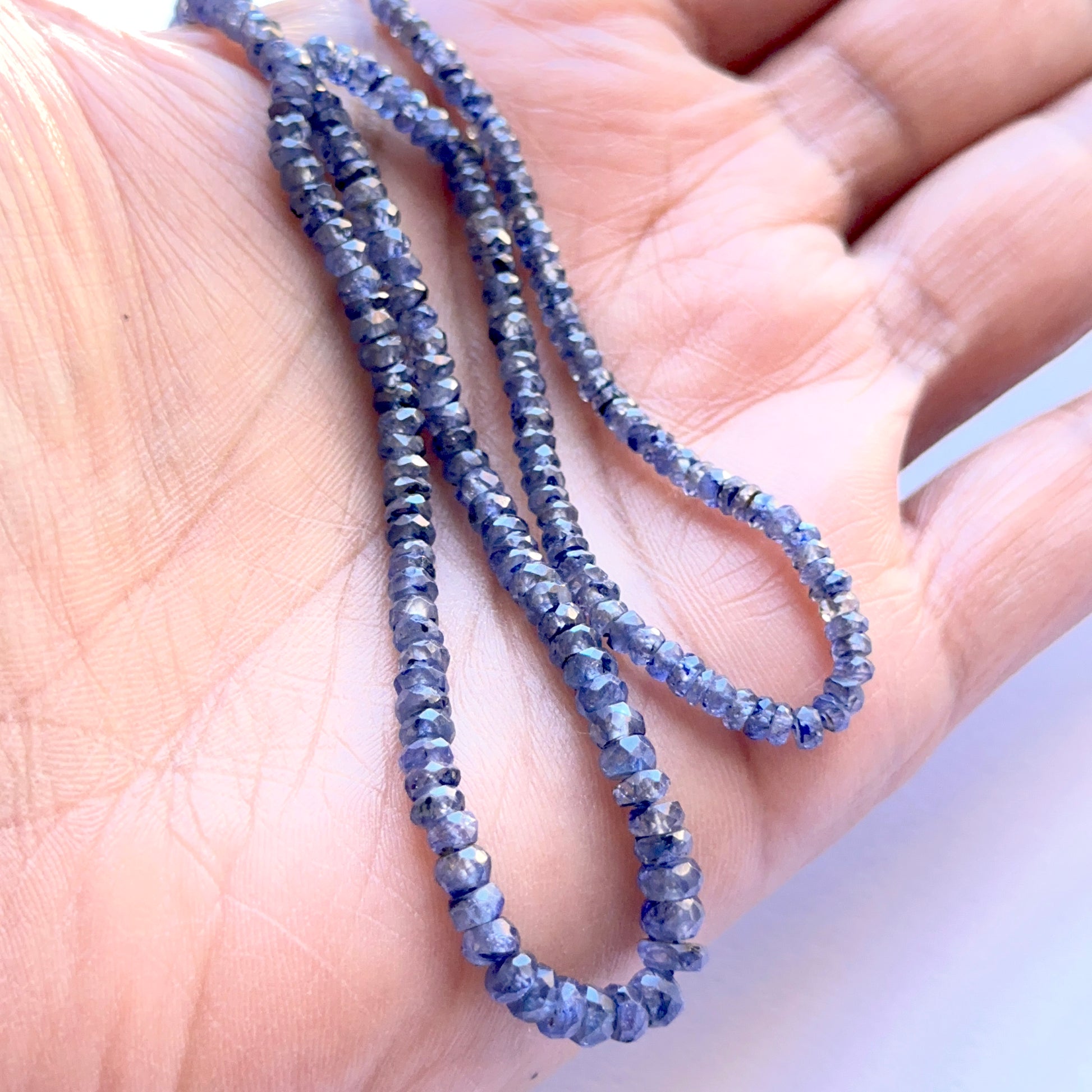 A person holds the Blue Sapphire faceted rondelle strand, showcasing rich blue tones and fine faceting.
