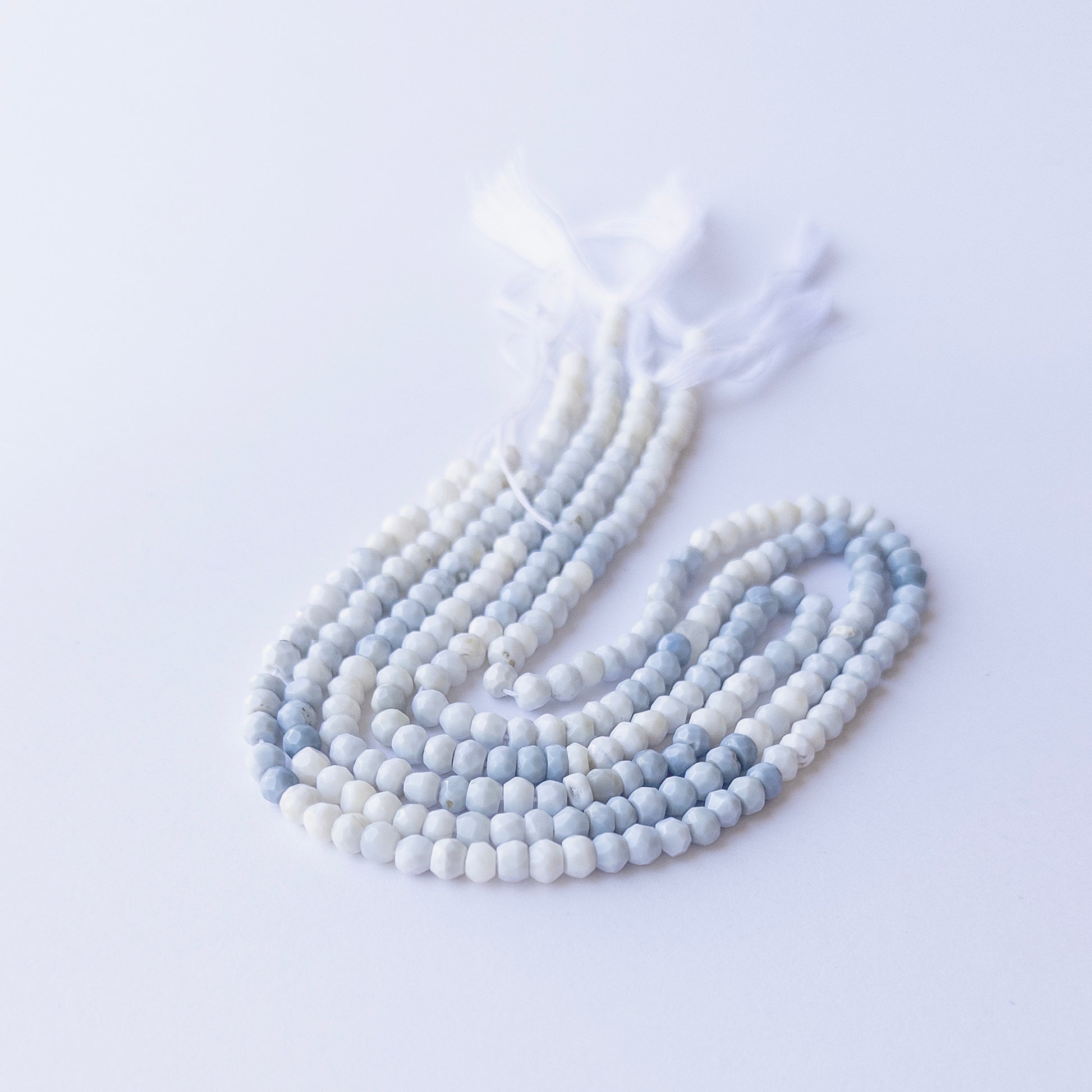 Strands of Denim Opal faceted rondelle gemstone beads arranged neatly, showcasing their fine cut and natural blue hues.