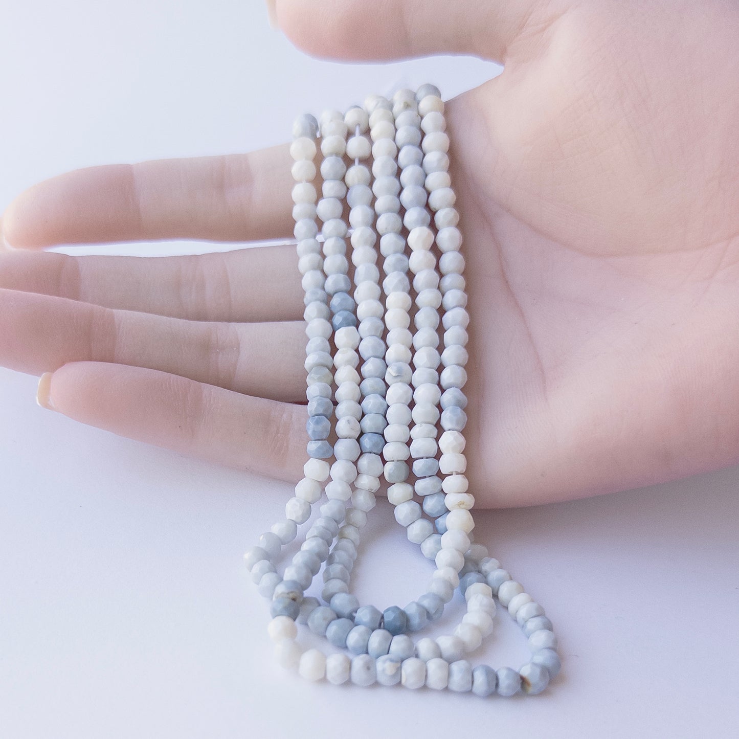 A person holds delicate strands of Denim Opal beads, showcasing their faceted rondelle design.