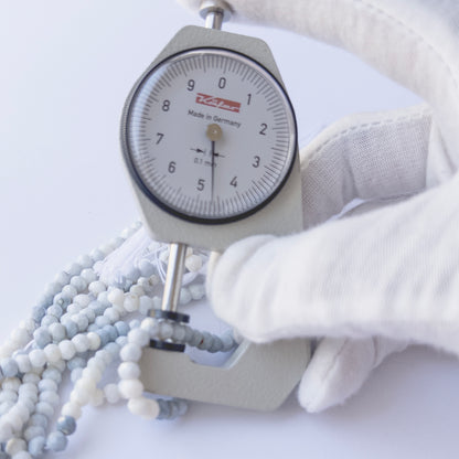 A dial gauge measures the Denim Opal faceted rondelle 4.6–4.7mm gemstone bead.