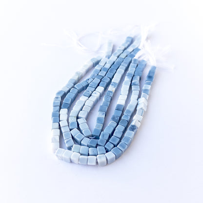 Denim Opal smooth cube gemstone beads in soft blue‑grey tones arranged on a 20cm strand for handmade jewellery components.