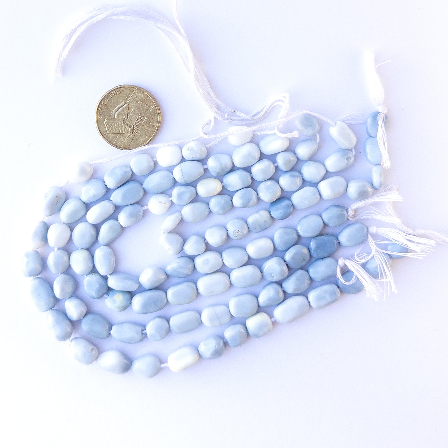 A coin is placed near delicate strands of Denim Opal beads for scale.