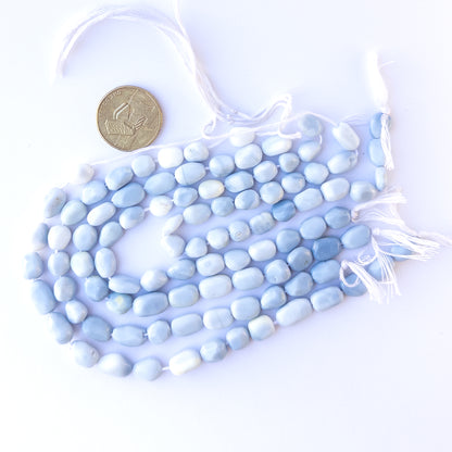 A coin is placed near delicate strands of Denim Opal beads for scale.