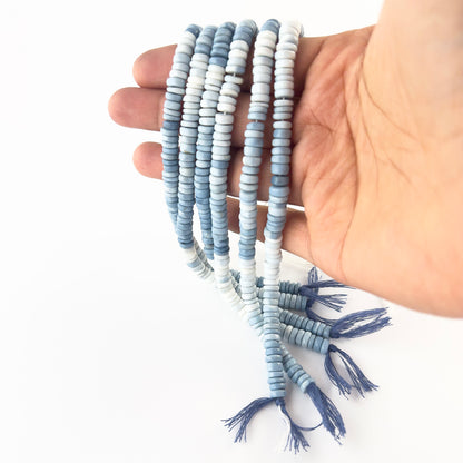 A person holds Denim Opal smooth wheel beads, showing their rounded design and denim‑blue colour.