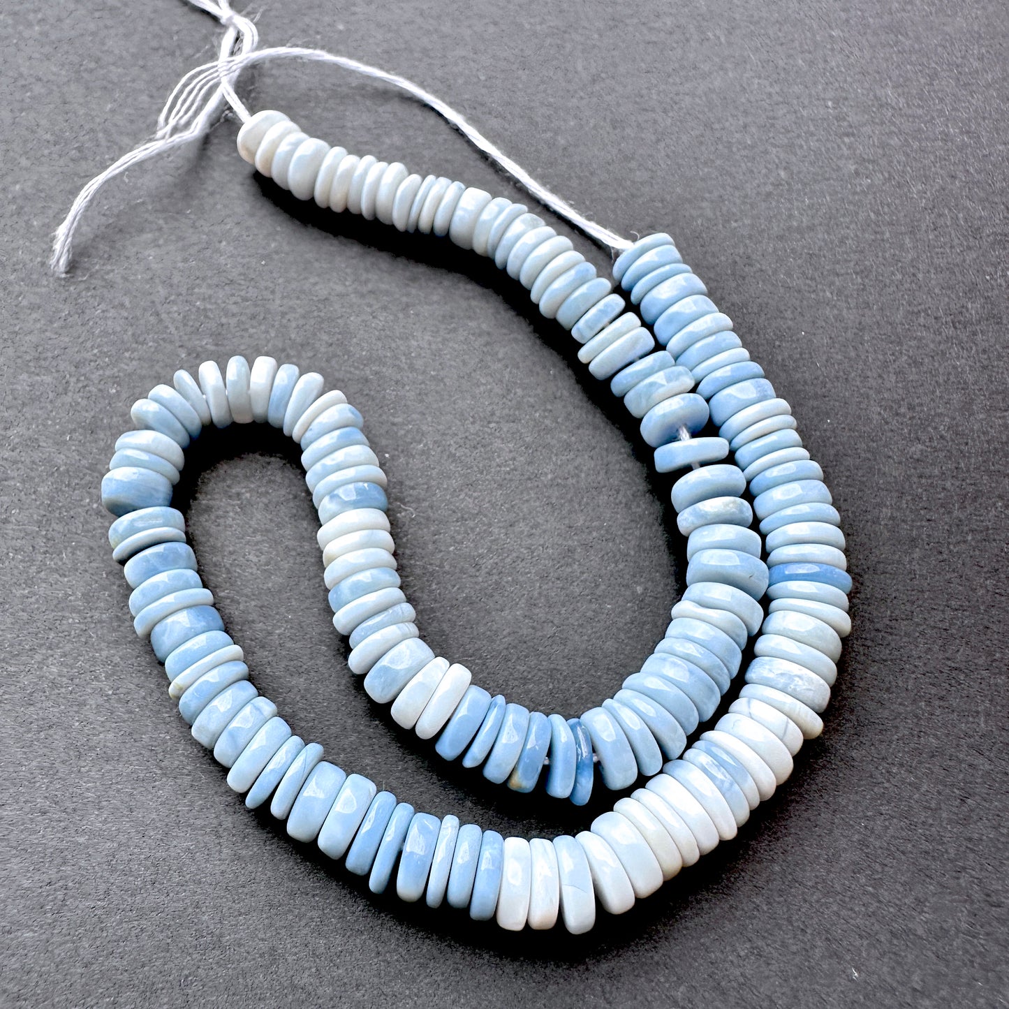 Denim Opal smooth wheel beads in soft blue tones arranged on a 22cm strand for handmade jewellery components.