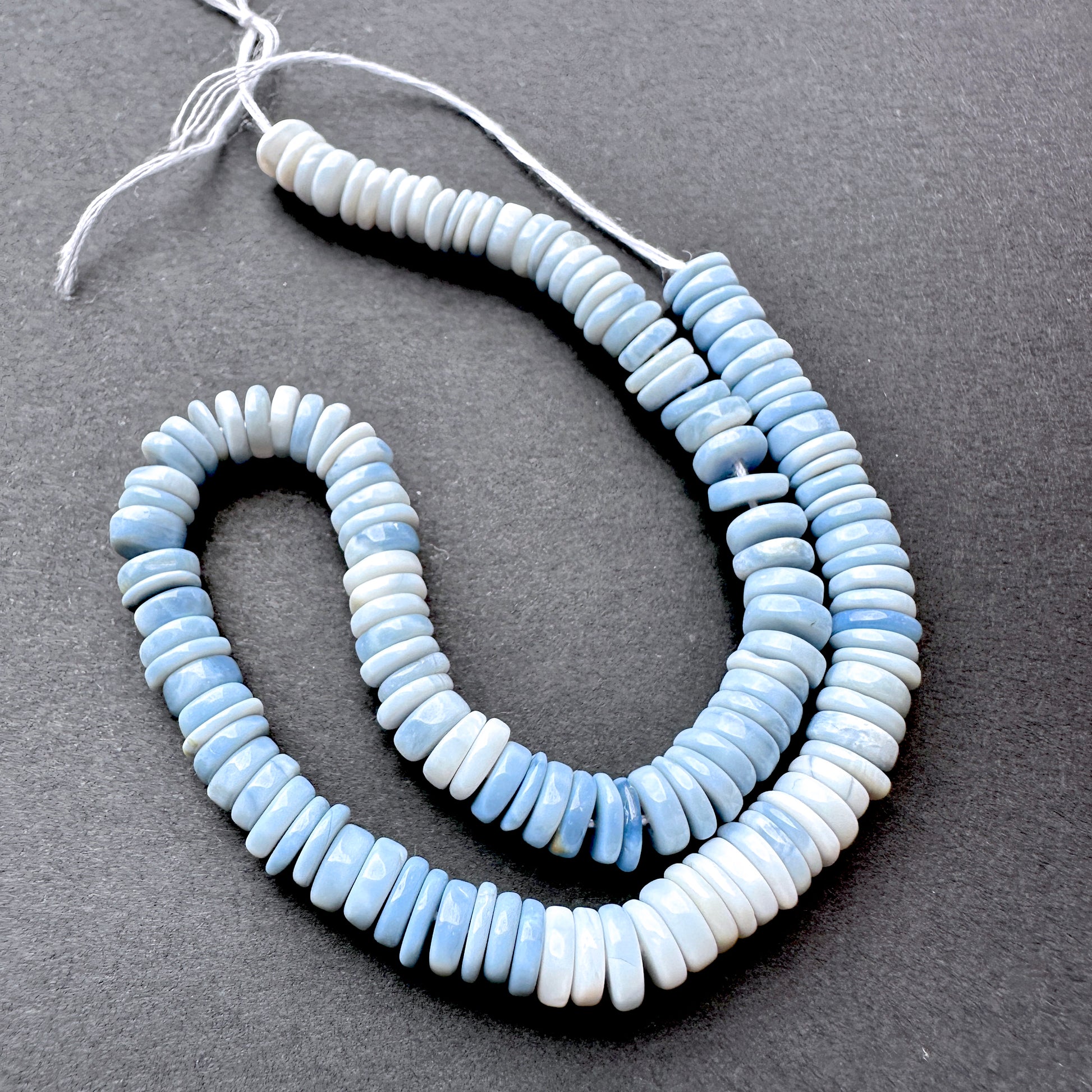 Denim Opal smooth wheel beads in soft blue tones arranged on a 22cm strand for handmade jewellery components.