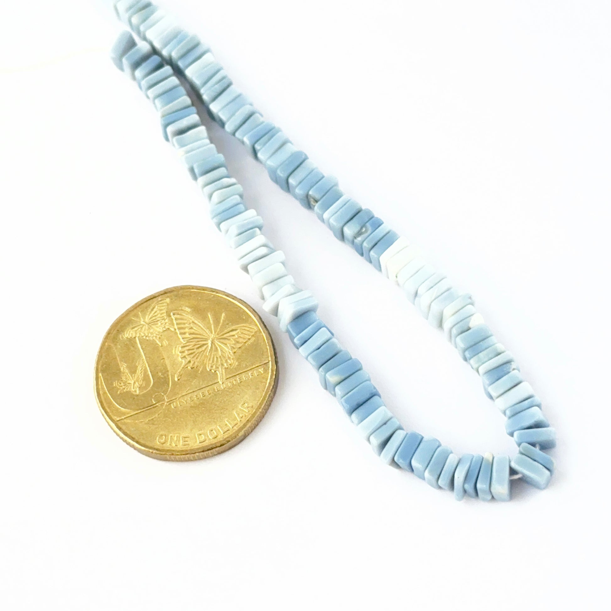 Hand‑selected Denim Opal beads showing muted blue shades and polished surfaces placed next to Australian dollar coin for scale.