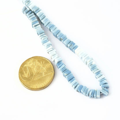 Hand‑selected Denim Opal beads showing muted blue shades and polished surfaces placed next to Australian dollar coin for scale.