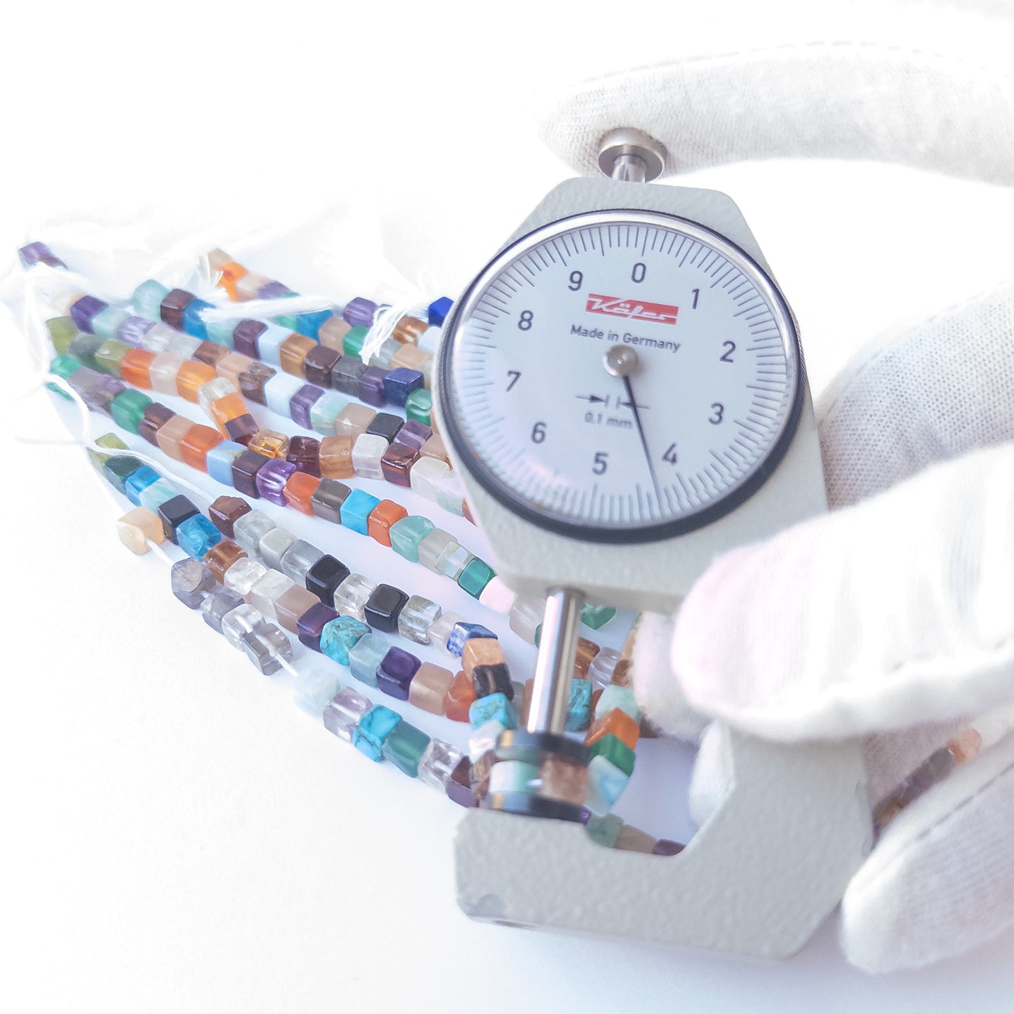 A person holds delicate strands of Disco beads, showcasing their smooth cube design.