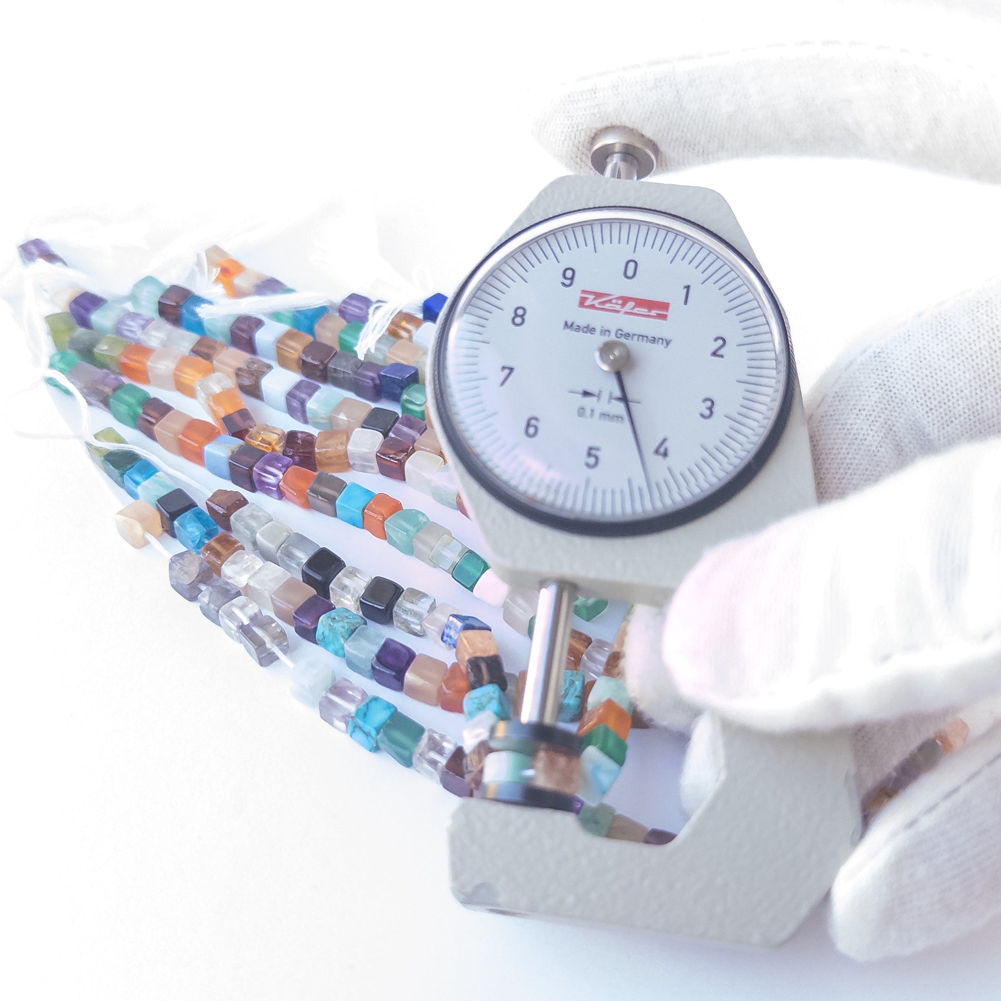 A person holds delicate strands of Disco beads, showcasing their smooth cube design.