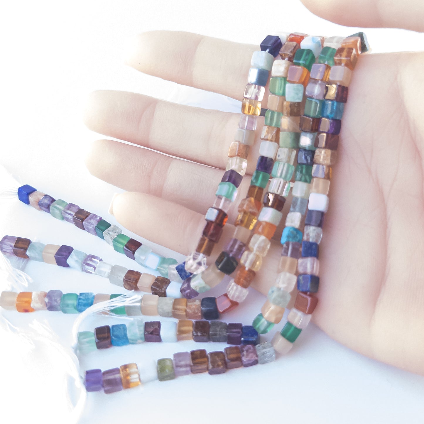 A person holds delicate strands of Disco beads, showcasing their smooth cube design.