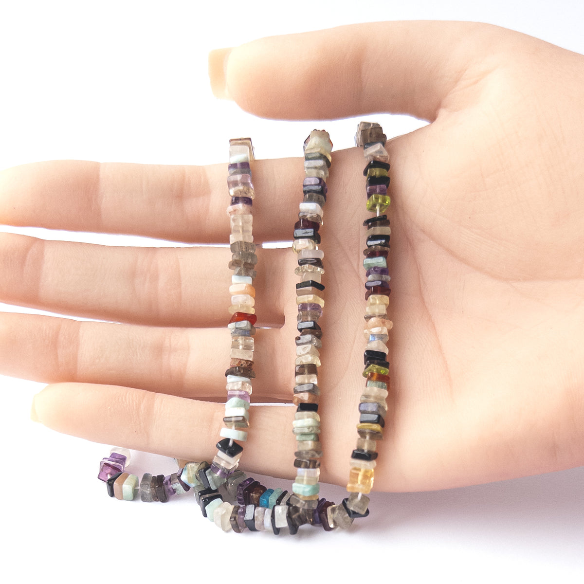 A person holds delicate strands of Disco beads, showcasing their smooth square Heishi design.