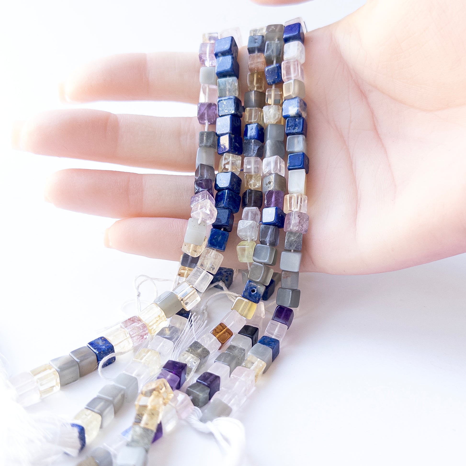 A person holds delicate strands of Disco beads, showcasing their smooth square design.