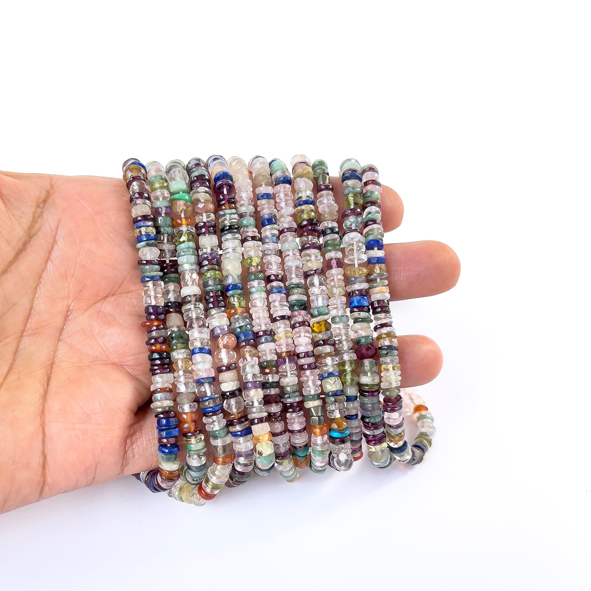 A person holds delicate strands of Disco smooth wheel heishi beads, showcasing their rounded design.