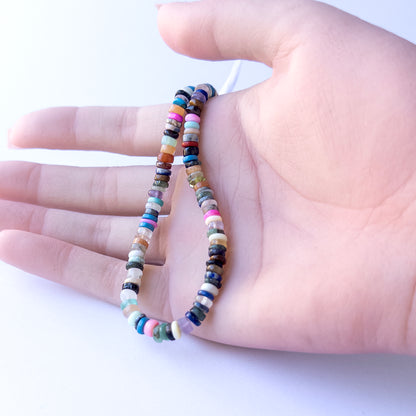 A person holds delicate strands of Disco smooth wheel heishi beads, showcasing their size and design.